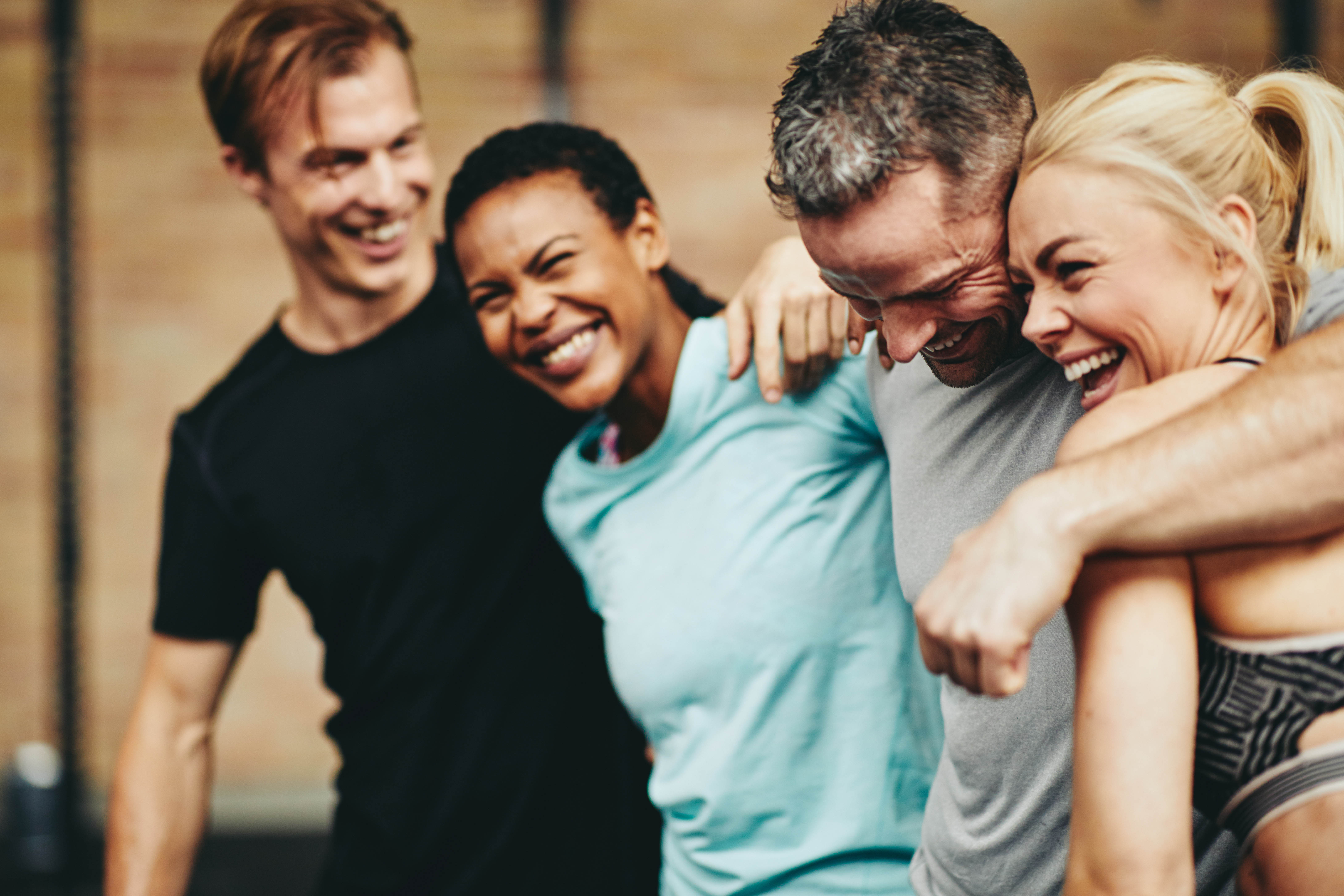 Diverse group of young men and women with their arms around each other and smiling in the gym